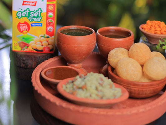 Traditional Indian snack setup with crispy pani puri balls, chutneys, and fillings in clay bowls on a terracotta plate